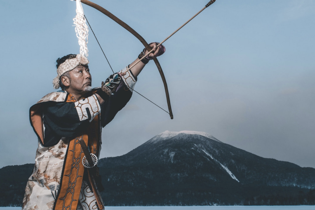 man wearing ainu clothes with bow and arrow