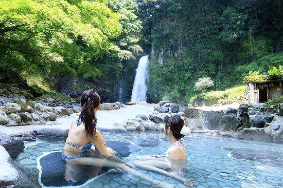 2 girls sitting in hot bath looking at waterfall