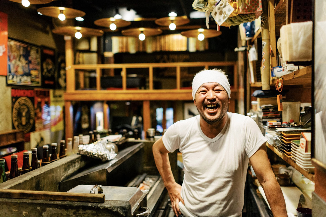 man with white headband standing in japanese izakaya