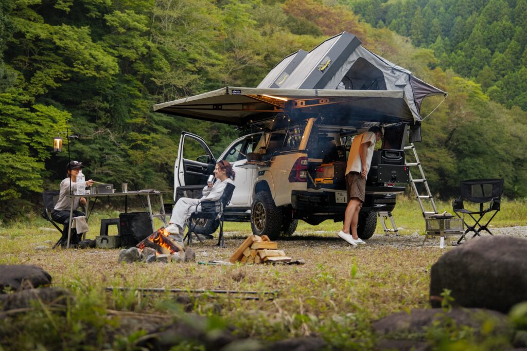 A Hilux camper with its awning out, chairs and a fire on the grass beside it