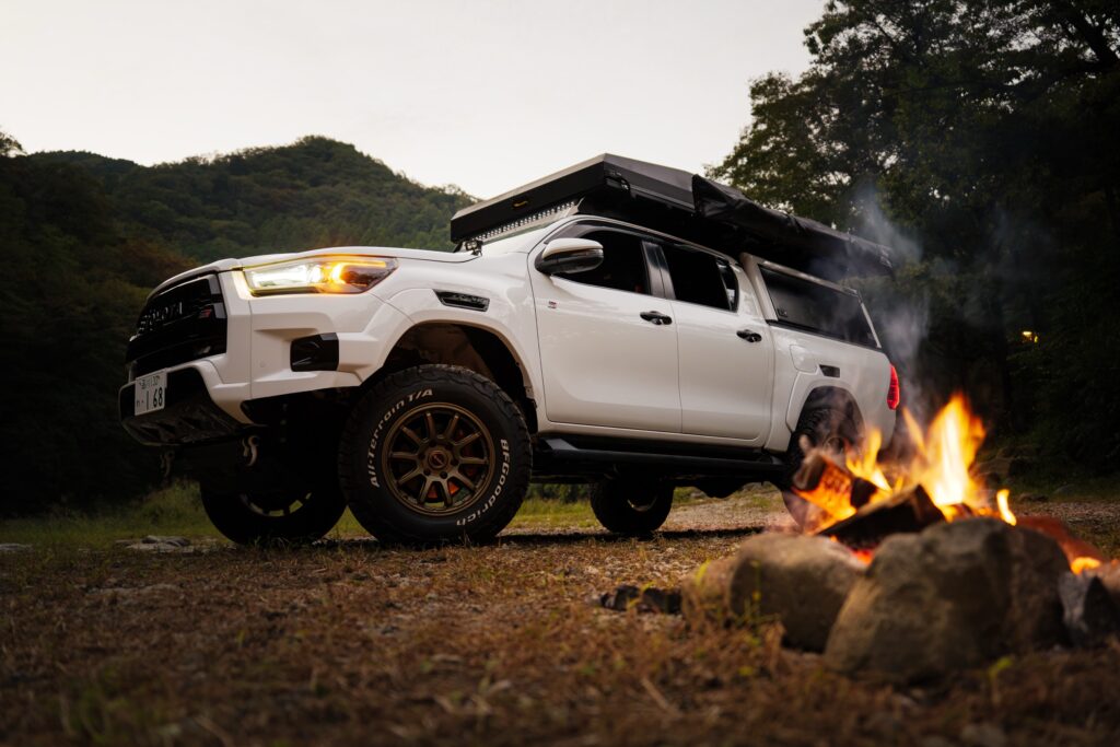 A Hilux camper with its rooftop tent up beside a campfire at dusk