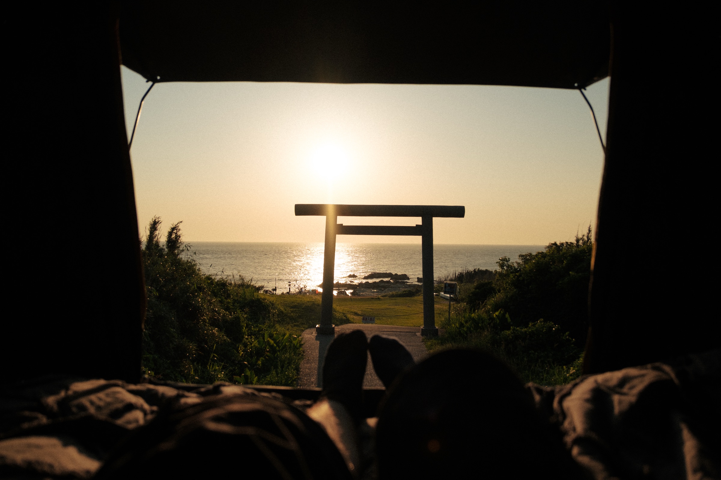 Sunset over the sea through a torii gate, seen from inside a rooftop tent