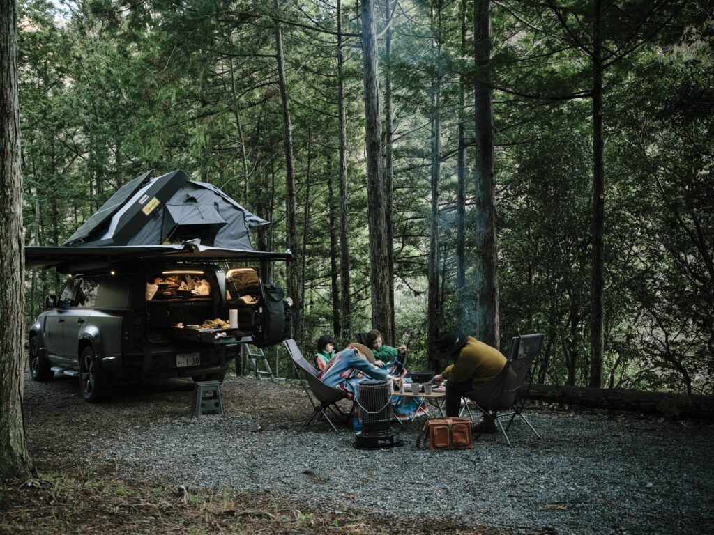森のオートキャンプ場の区画に停まるLand Rover Defenderのキャンピングカー。チェアとテーブルが出してある