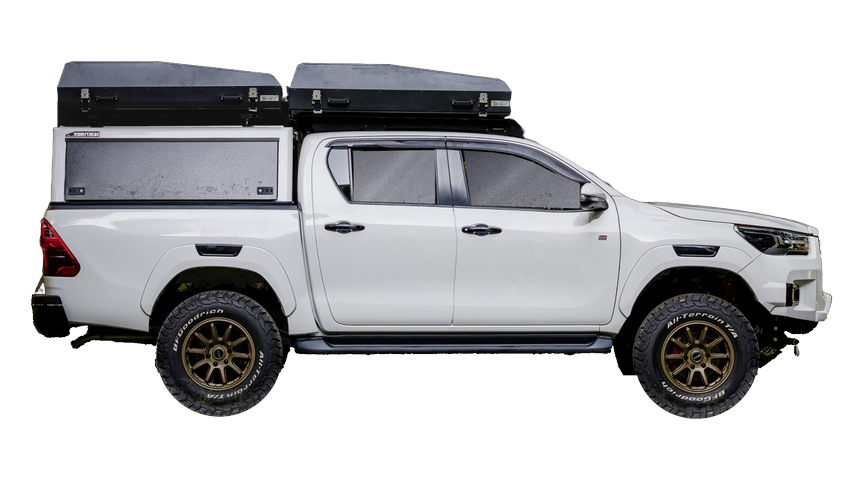 Side view of a white Toyota Hilux with a canopy and two folded rooftop tents, bronze wheels and all-terrain tyres
