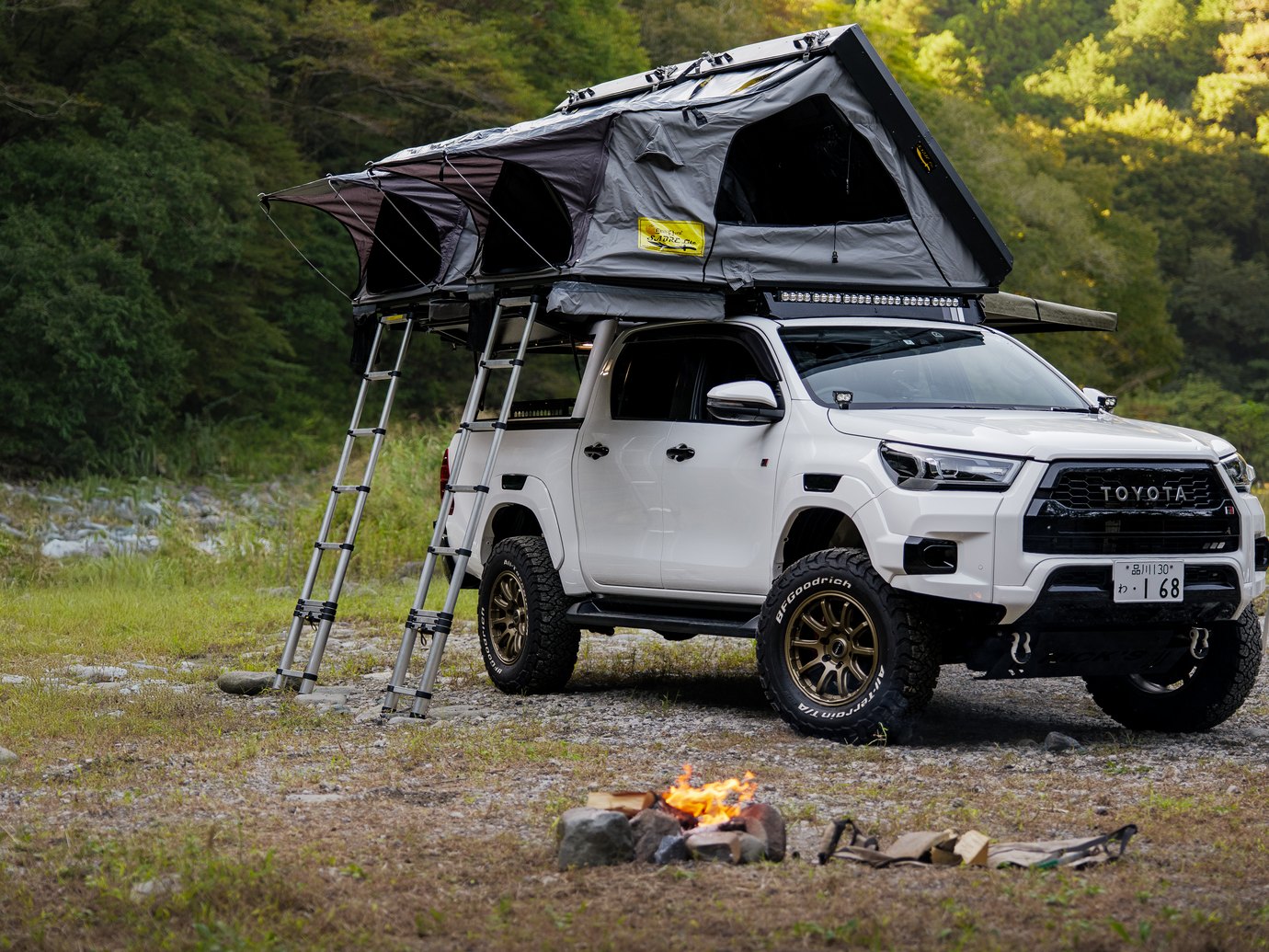 2つのルーフテントを広げてはしごを下ろしたHilux、手前で燃える焚き火