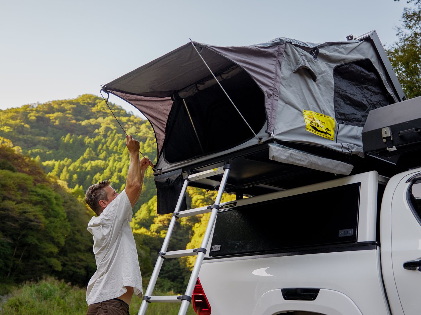 伸縮式のはしごを伸ばし、Hiluxのキャノピーの上のルーフテントを開く男性