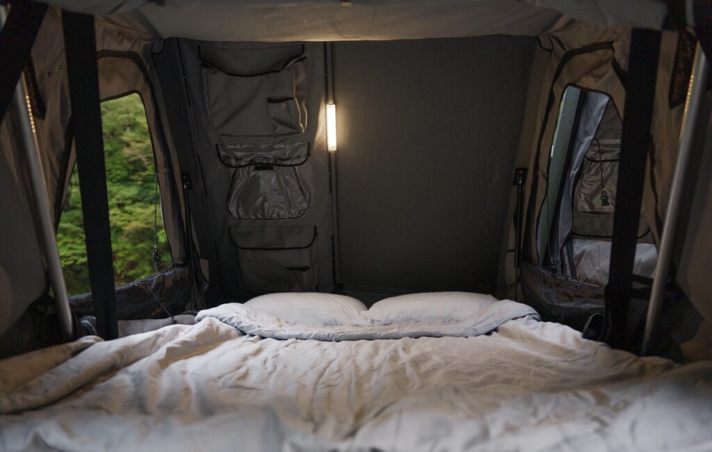A made bed inside a rooftop tent: pillows, duvet and a reading light