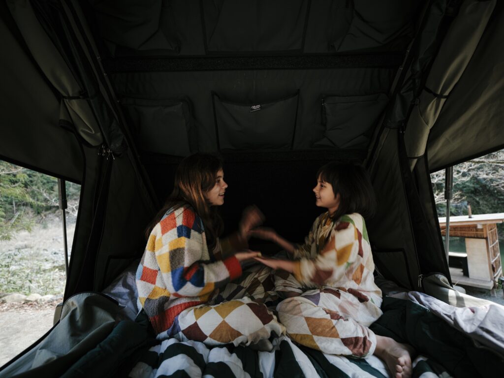 Two people wrapped in blankets, talking inside a rooftop tent