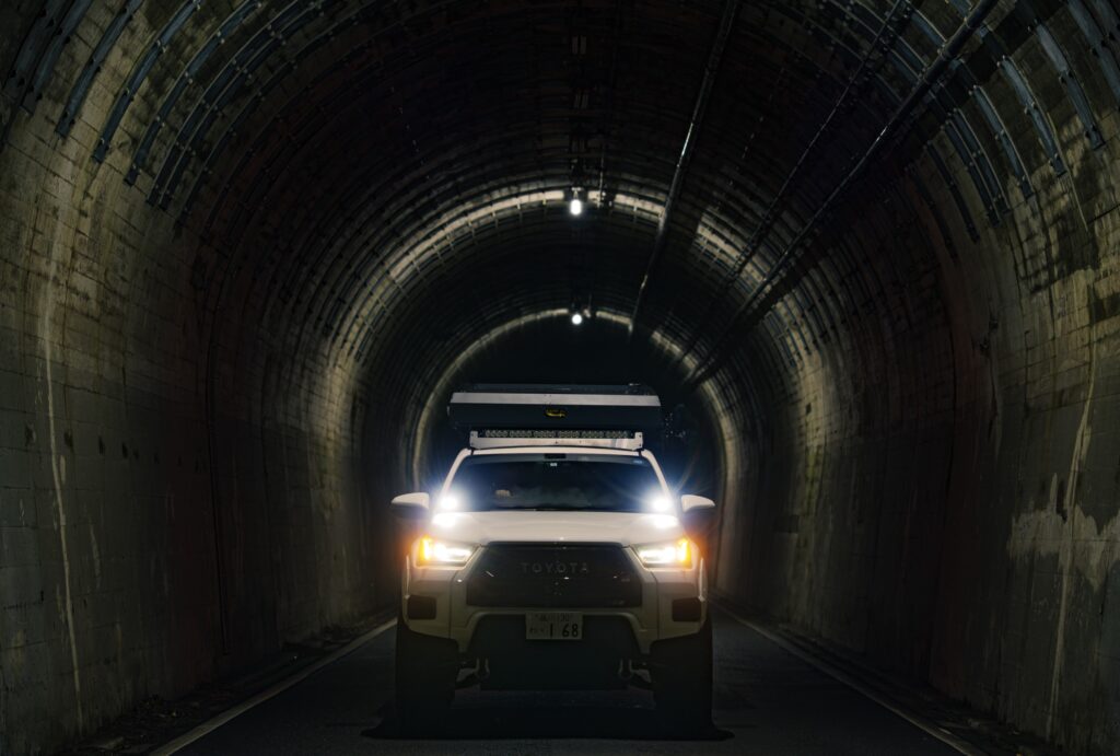 A Hilux camper's headlights coming through a dark mountain tunnel