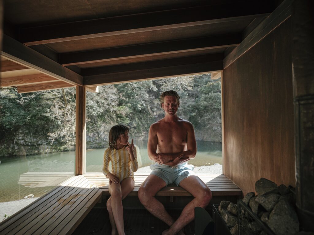 Two people warming up in a wooden bath house open to a river