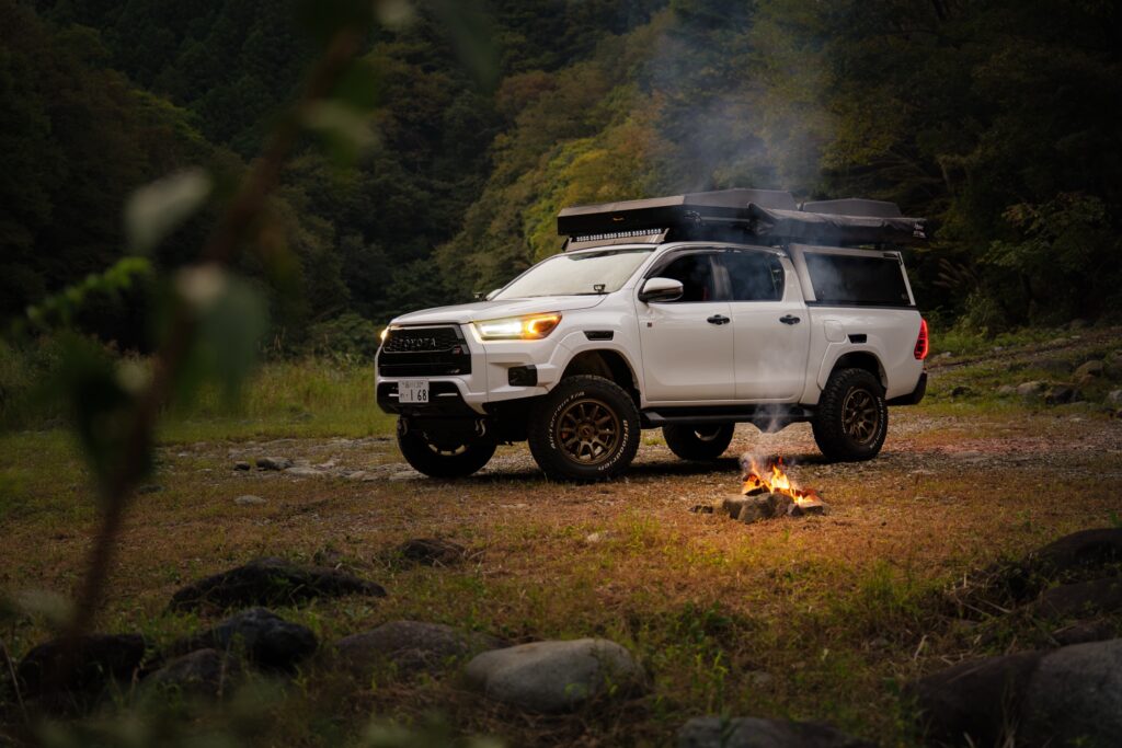 A Hilux camper parked for the night at dusk, a small fire beside it